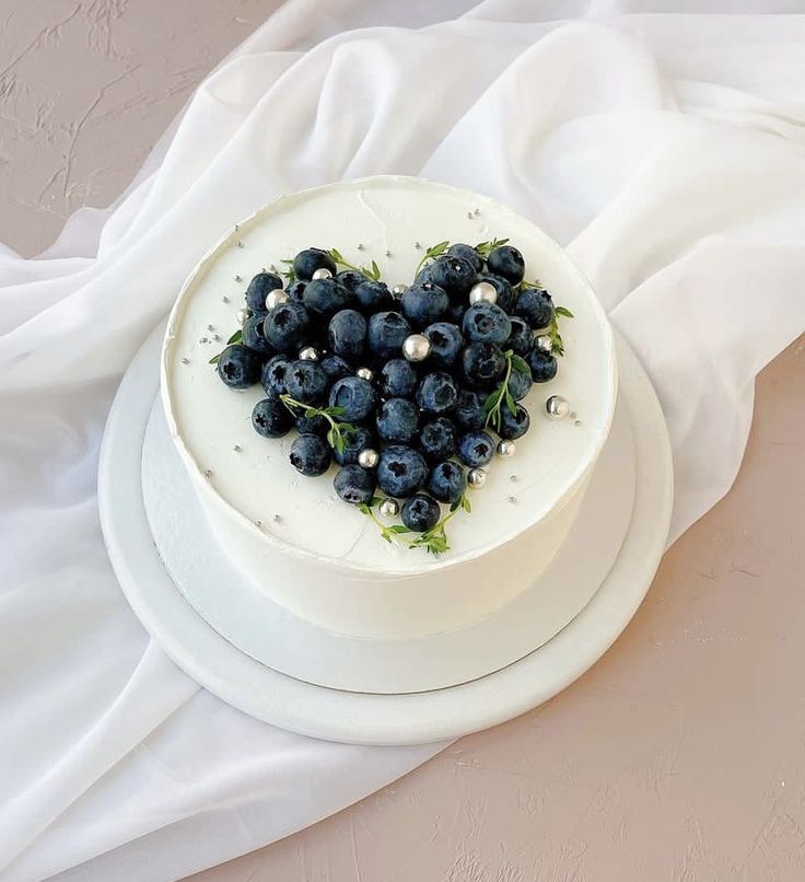 a white cake topped with blueberries on top of a white cloth covered tablecloth