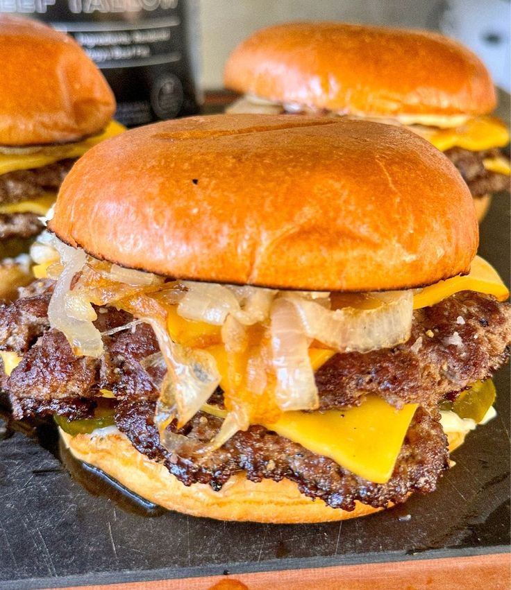 three cheeseburgers with meat and onions on a cutting board