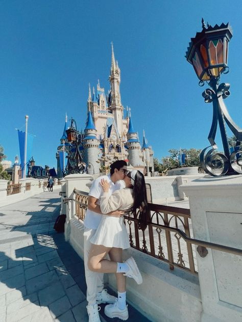 a man and woman kissing in front of the castle at disney world on a sunny day