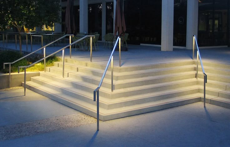 the stairs are lit up at night in front of a building with glass doors and windows