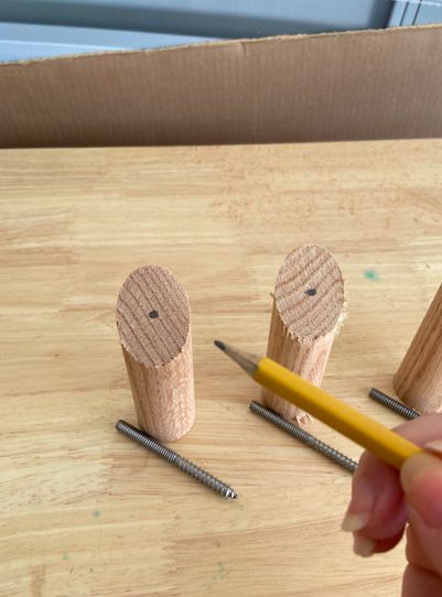 a person holding a pencil in front of wooden pegs and two small pieces of wood