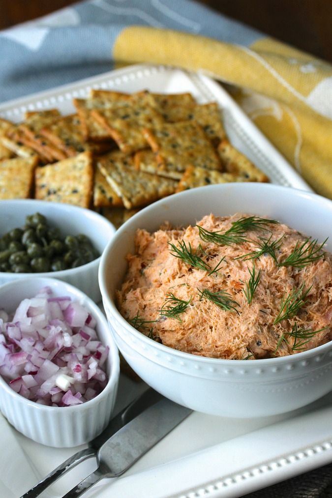 a white plate topped with bowls filled with food next to crackers and olives