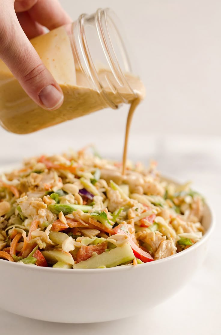 someone pouring dressing into a white bowl filled with salad