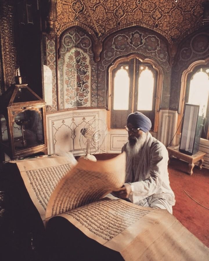 an old man sitting on the floor reading a book in a room with stained glass windows