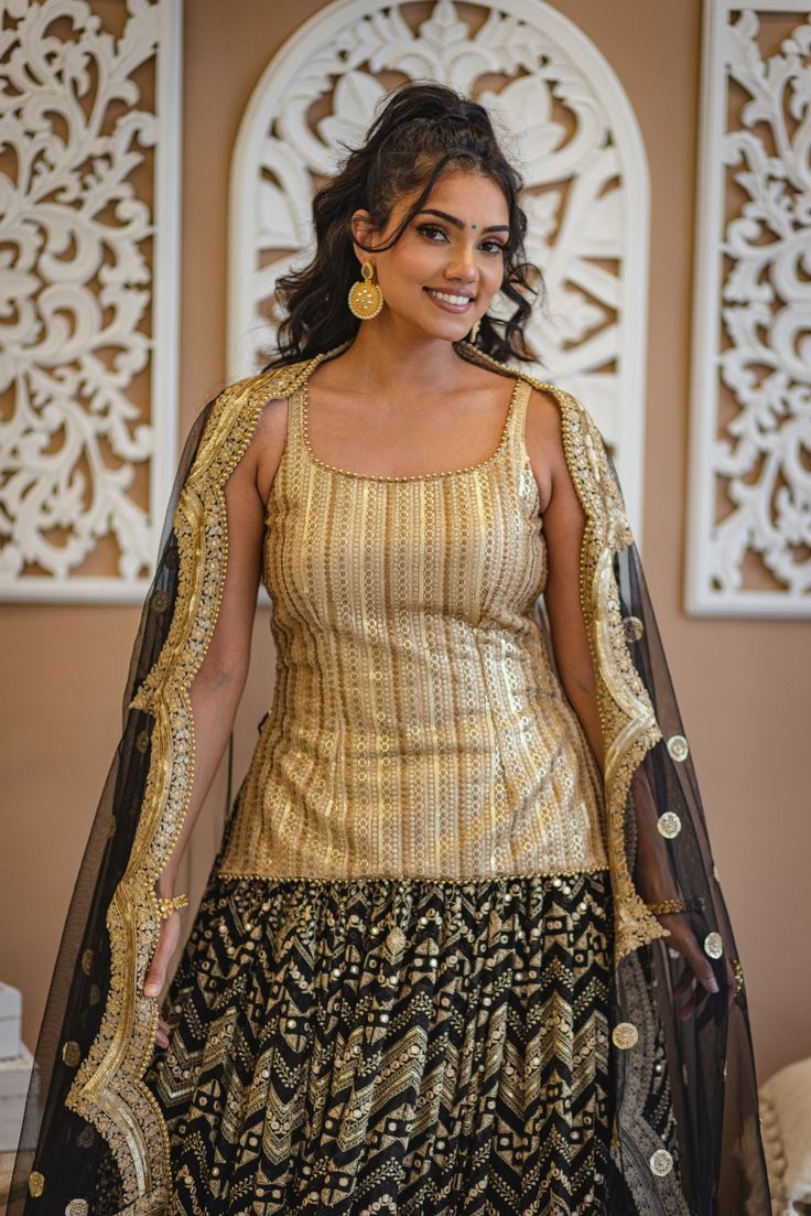 Loyla - Black Georgette Lengha & Gold Silk Choli w/ Mirror & Bead Embroidery If elegance had to be visually depicted then this black and gold lehenga choli would speak volumes with its sophistication! Gold dupion silk choli w/ sequins & bead handwork Breathable golden Dupion silk blouse Graceful scoop neckling choli blouse Beaded trim detail at neck & hemline Gorgeous sequin & bead embroidery Sweetheart back neck with tie-up Dori Flowy black georgette lehenga w/ mirror embroi Anarkali Sharara With Gold Embroidery For Party, Gold Art Silk Sharara For Party, Gold Palazzo Set For Party Festivals, Bollywood Black Palazzo Set For Reception, Festive Sharara With Gold Embroidery For Navratri, Festive Gold Embroidered Sharara For Navratri, Party Gold Art Silk Sharara, Gold Art Silk Lehenga For Party, Gold Chinon Sharara For Party