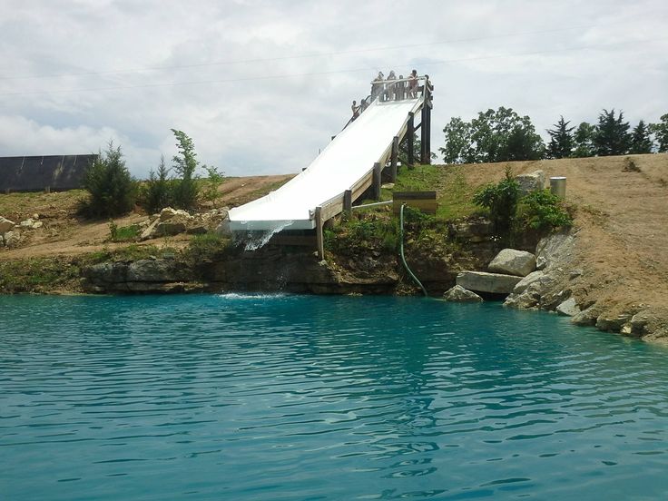 a slide going down the side of a hill into a body of water with people standing on it