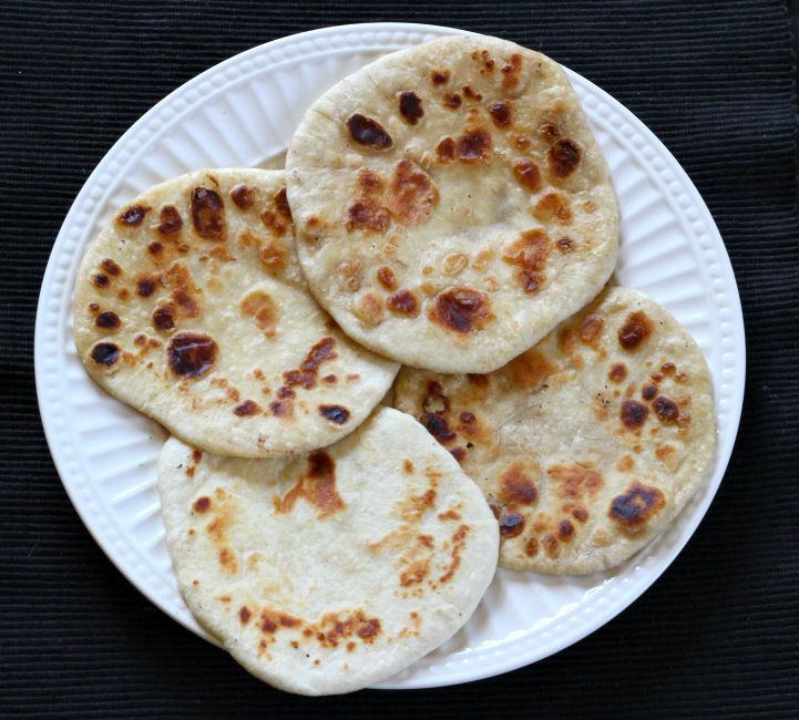 four flat breads on a white plate sitting on a black tablecloth, ready to be eaten