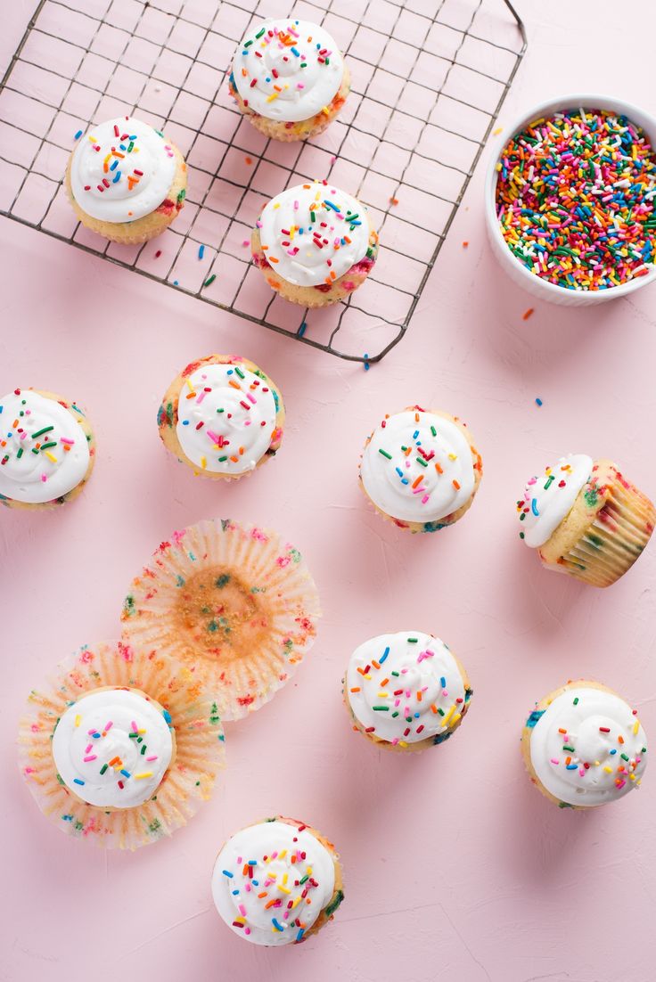 cupcakes with white frosting and sprinkles on a cooling rack