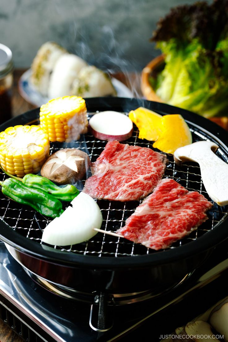 an outdoor grill with meat, vegetables and corn on the cob is shown in this image