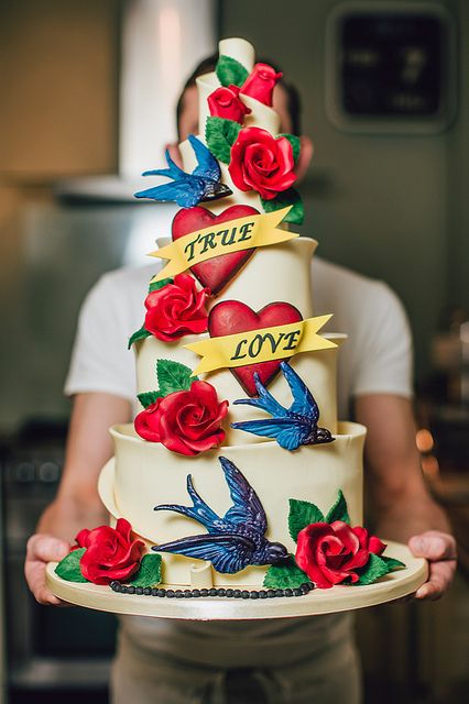 a man is holding a cake decorated with roses and birds on it that says true love