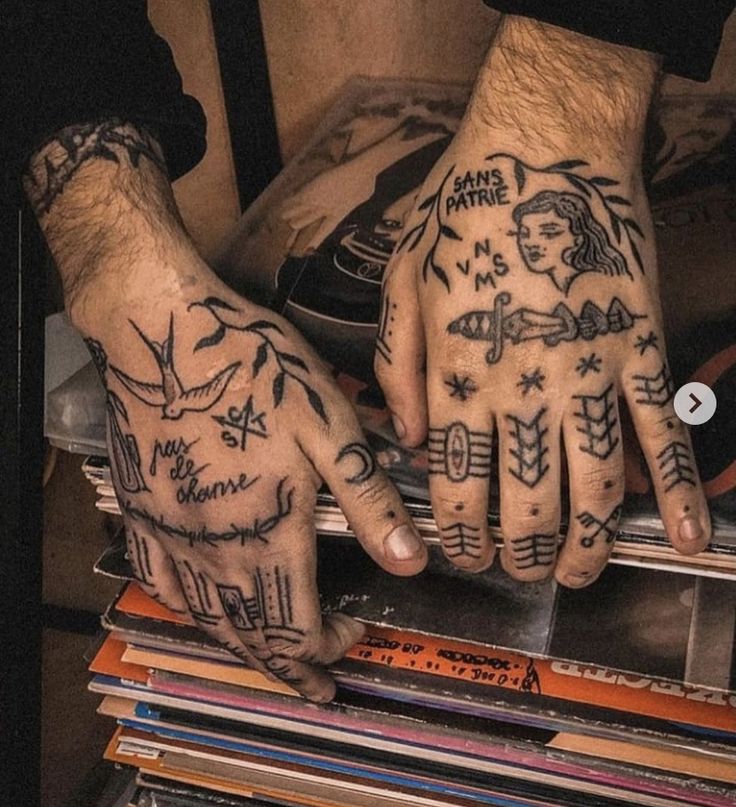 two hands with tattoos on them are sitting next to some books and cds in a pile