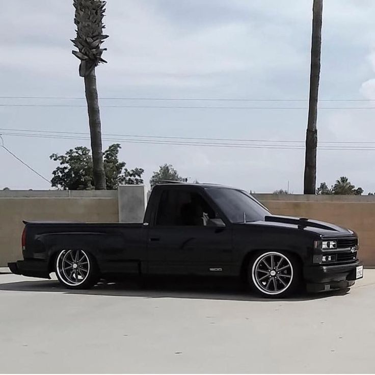 a black truck parked in a parking lot next to a palm tree and concrete wall