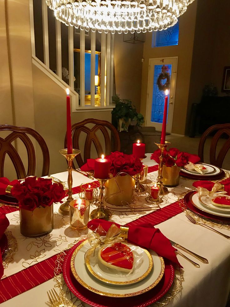 a dining room table is set with red and gold plates, silverware, and candles