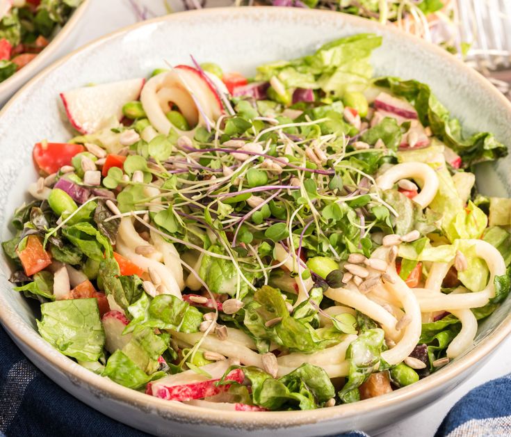 a white bowl filled with salad on top of a blue table cloth next to silverware