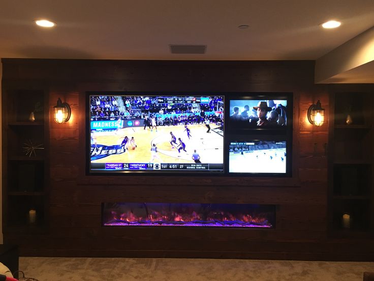 two large televisions mounted on the wall in a living room with fireplace and entertainment center