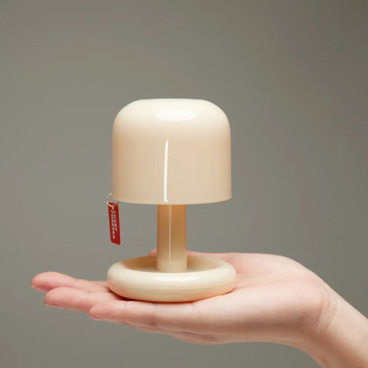 a hand holding a small lamp on top of a white base with a red tag