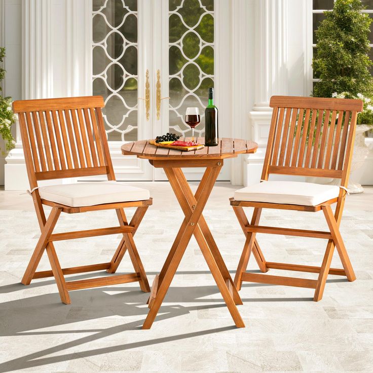 two wooden chairs sitting next to each other near a table with food and wine on it