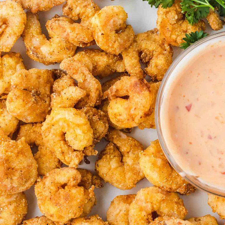 a white plate topped with fried tater tots next to a bowl of dipping sauce