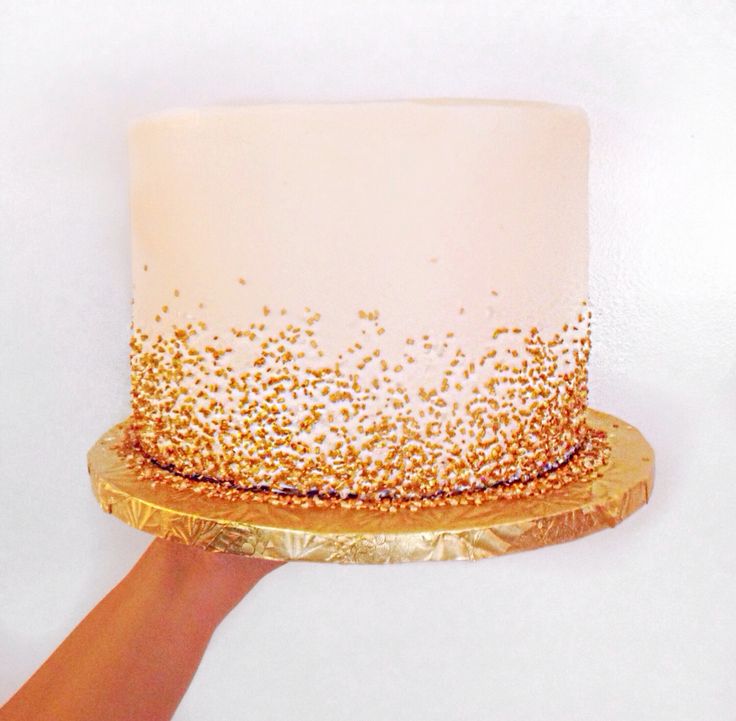 a hand holding a cake with gold sprinkles on it and white frosting