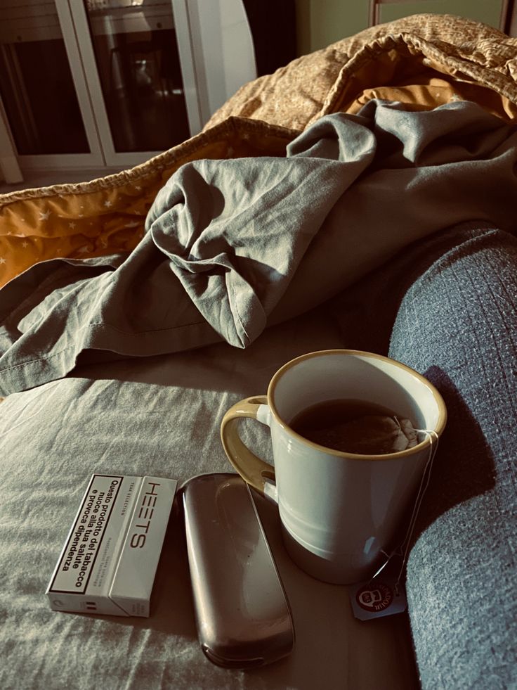 a cup of coffee sitting on top of a bed next to a cell phone