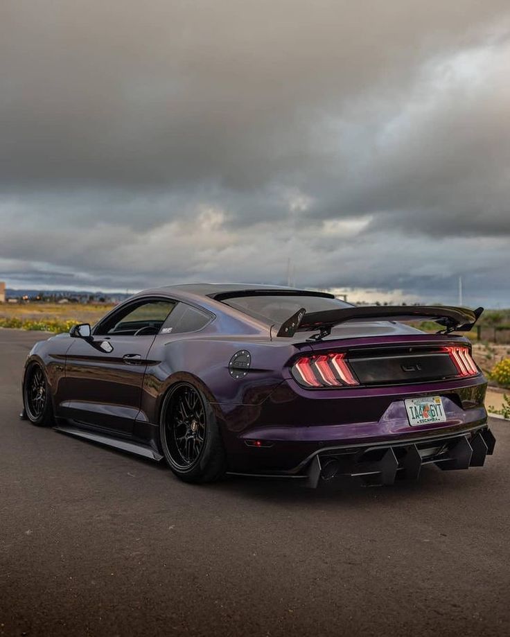 the rear end of a purple sports car parked in a parking lot with dark clouds overhead