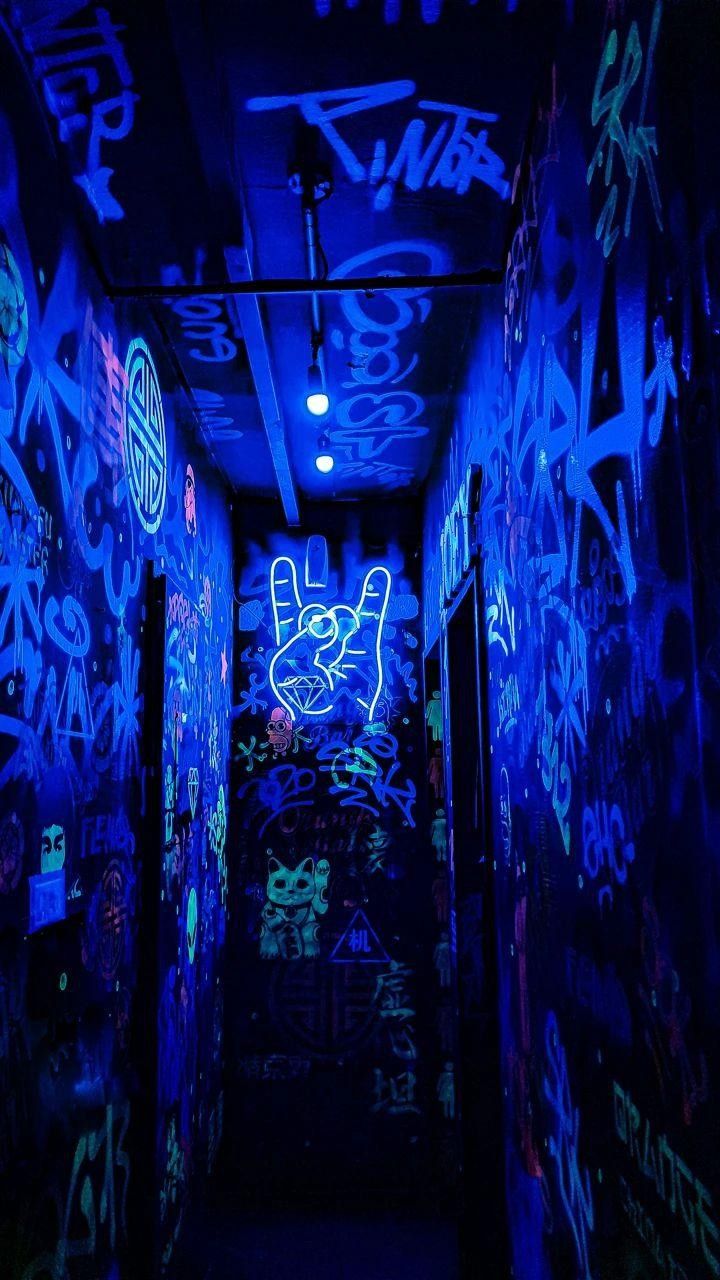 a dark hallway with graffiti all over the walls and floor, lit by blue lights