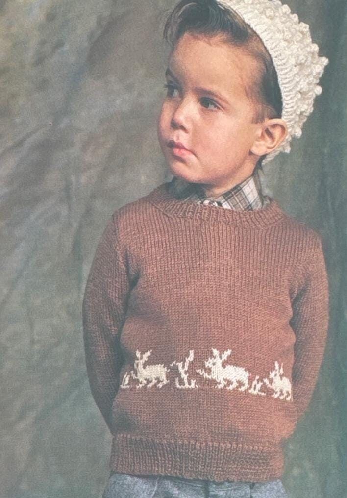 a young boy wearing a brown sweater with reindeers on it and a white knitted hat