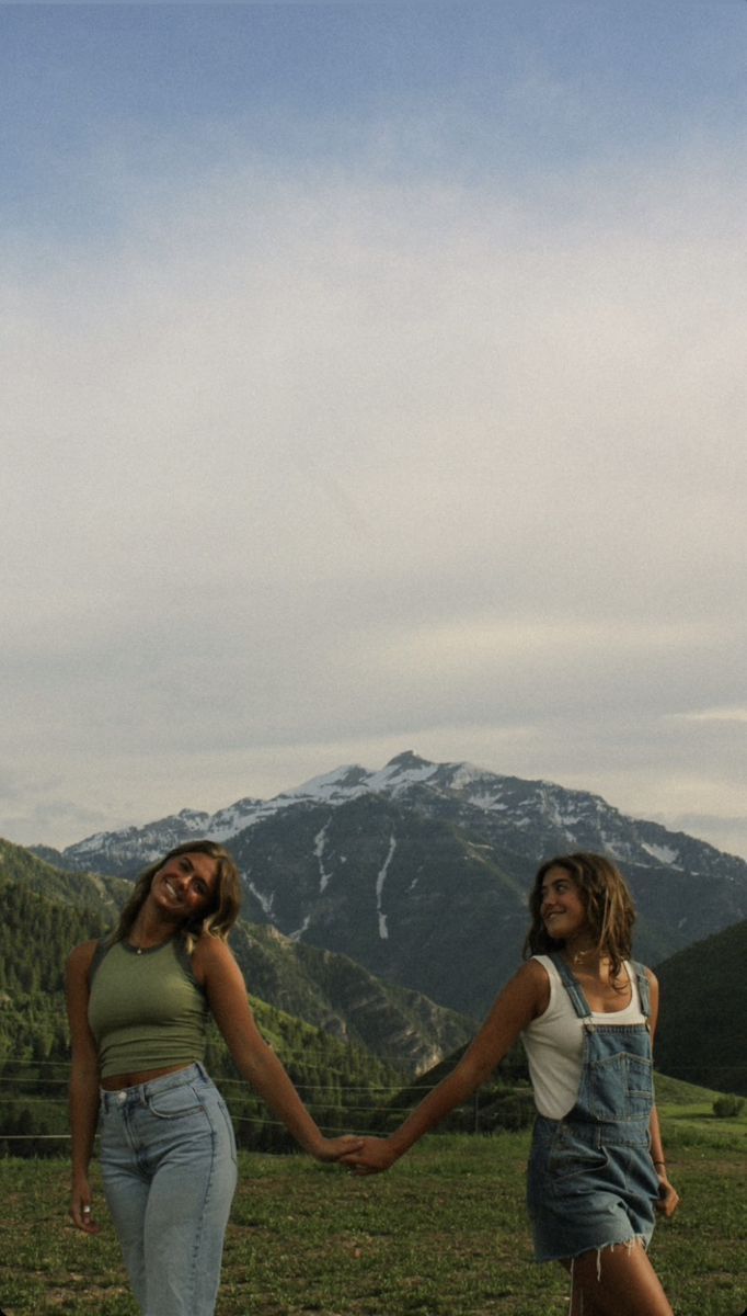 two women holding hands in front of mountains