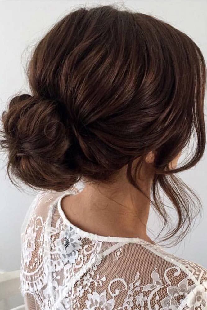 a woman with her hair in a low bun, wearing a white lace top and looking off to the side