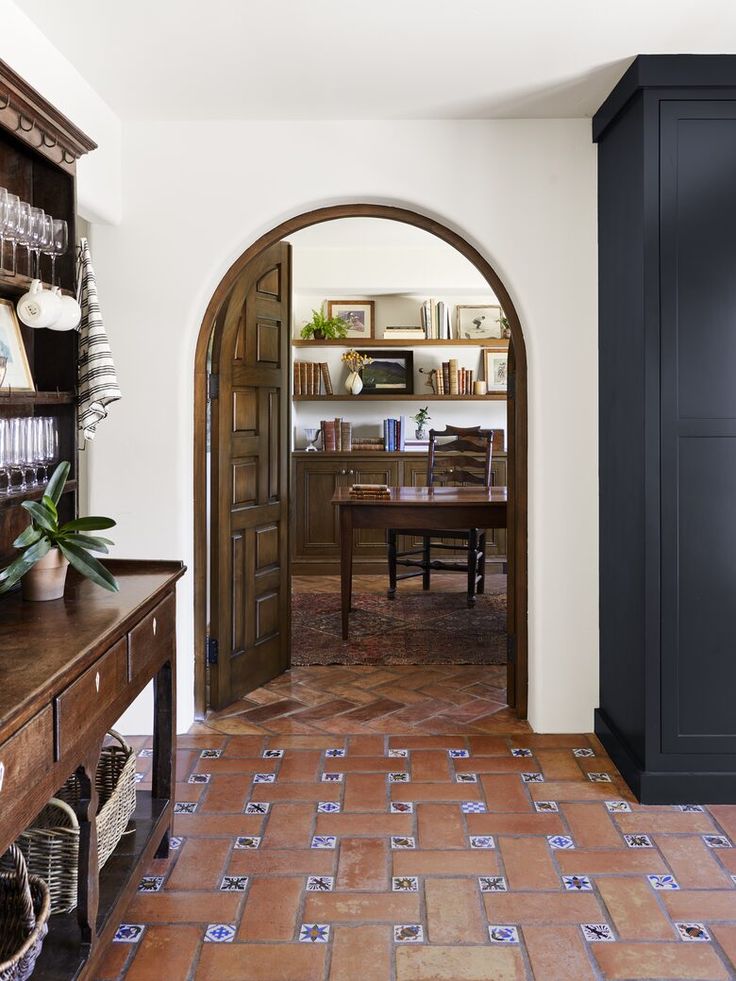 an arched doorway leads into a dining room with tile flooring and wooden table in the center