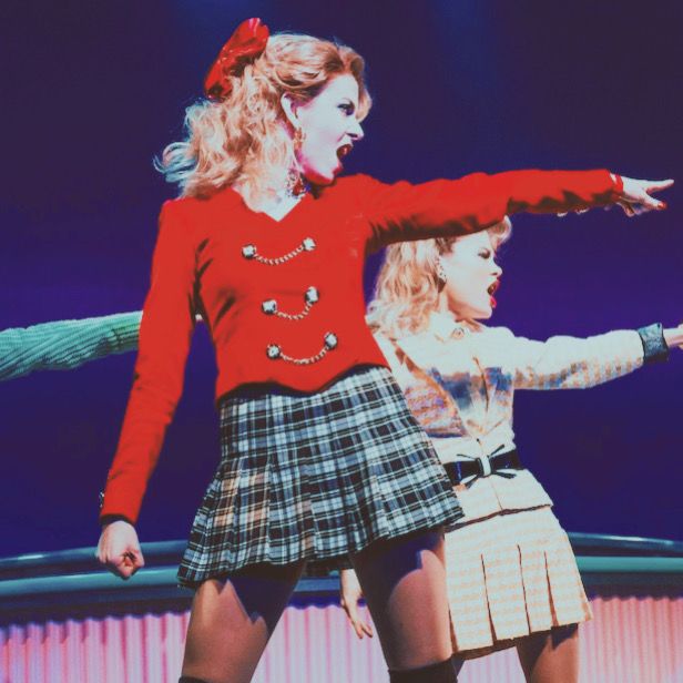 two young women dressed in plaid skirts and red sweaters, one holding her arms out to the side