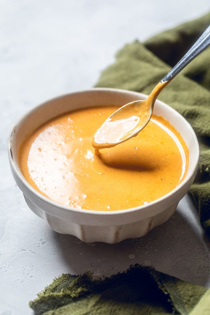 a spoon in a white bowl filled with orange colored sauce on a green cloth napkin