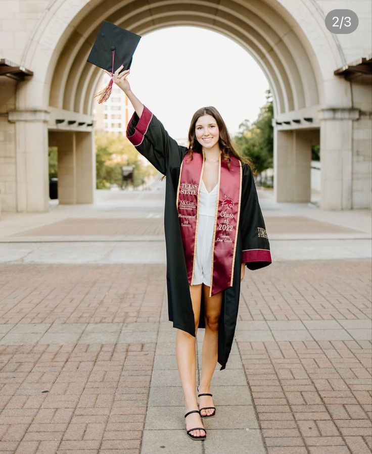 a woman wearing a graduation gown and holding up her diploma in front of an archway