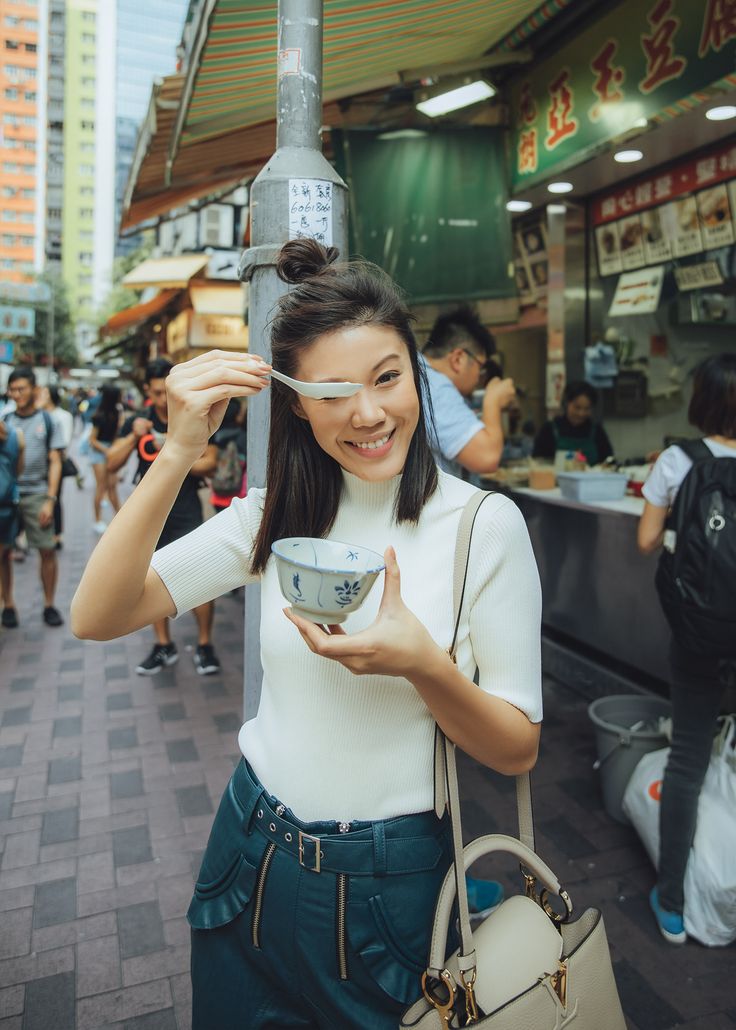 a woman holding up a bowl in front of a street pole with people walking around