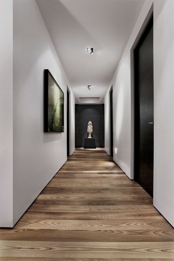 an empty hallway with paintings on the wall and wooden floors in front of it, along with black doors