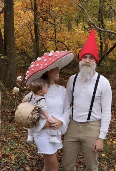 a man and woman dressed up as gnomes in the woods with a child on their lap