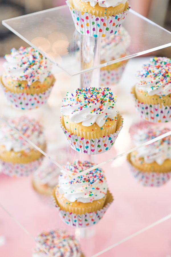 cupcakes with white frosting and sprinkles on a clear cake stand