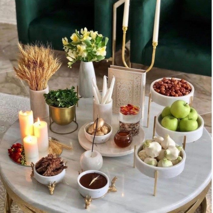 a table topped with bowls filled with food next to two green velvet chairs and candles