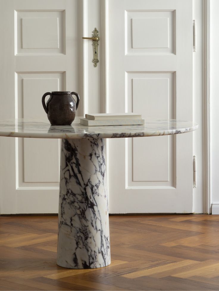 a marble table with a vase on it in front of a white door and wooden floors