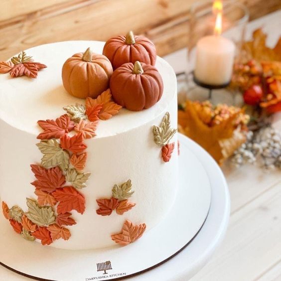 a white cake decorated with fall leaves and pumpkins