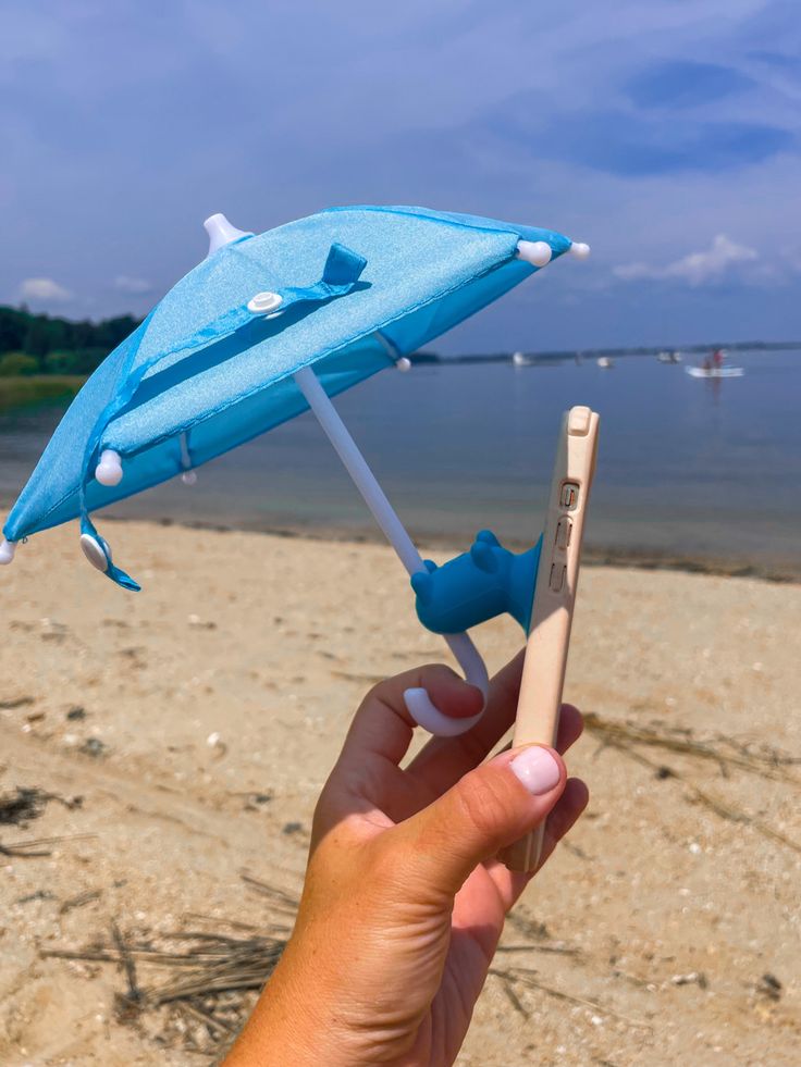 a person is holding an umbrella on the sand at the beach with water in the background