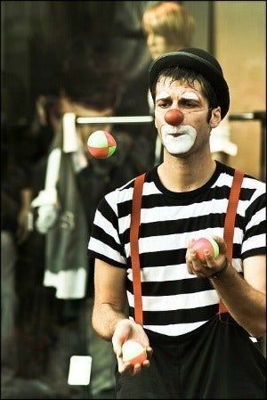 a man with clown makeup juggling balls in front of him and looking at the camera