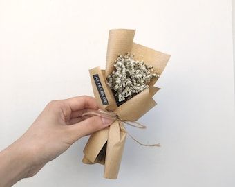 a hand holding a bouquet of dried flowers in it's wrapper with string