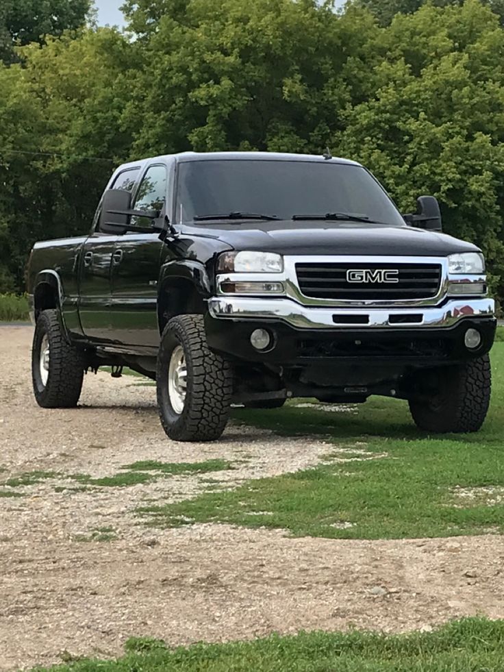 a large black truck parked on top of a dirt road next to green grass and trees