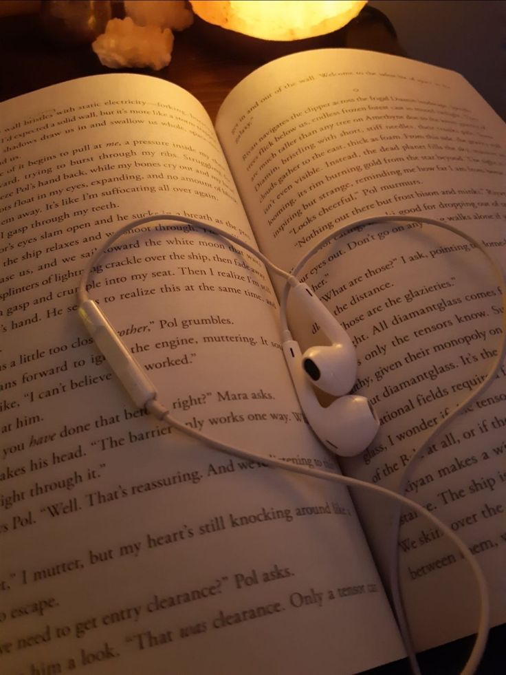 an open book with headphones on top of it and a lit candle in the background