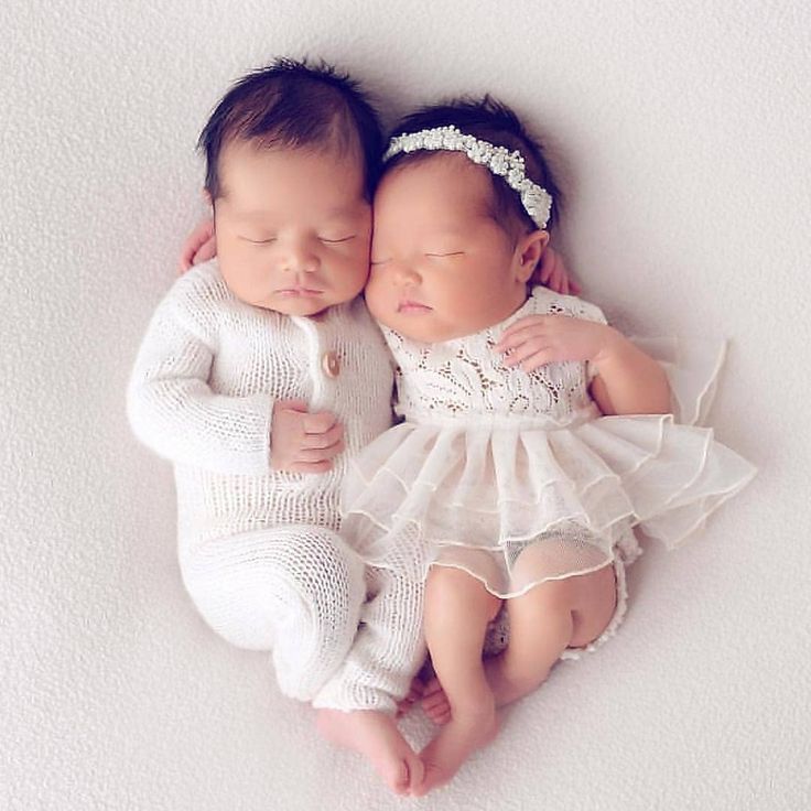 two babies are laying next to each other on a white surface, one is holding the baby's head