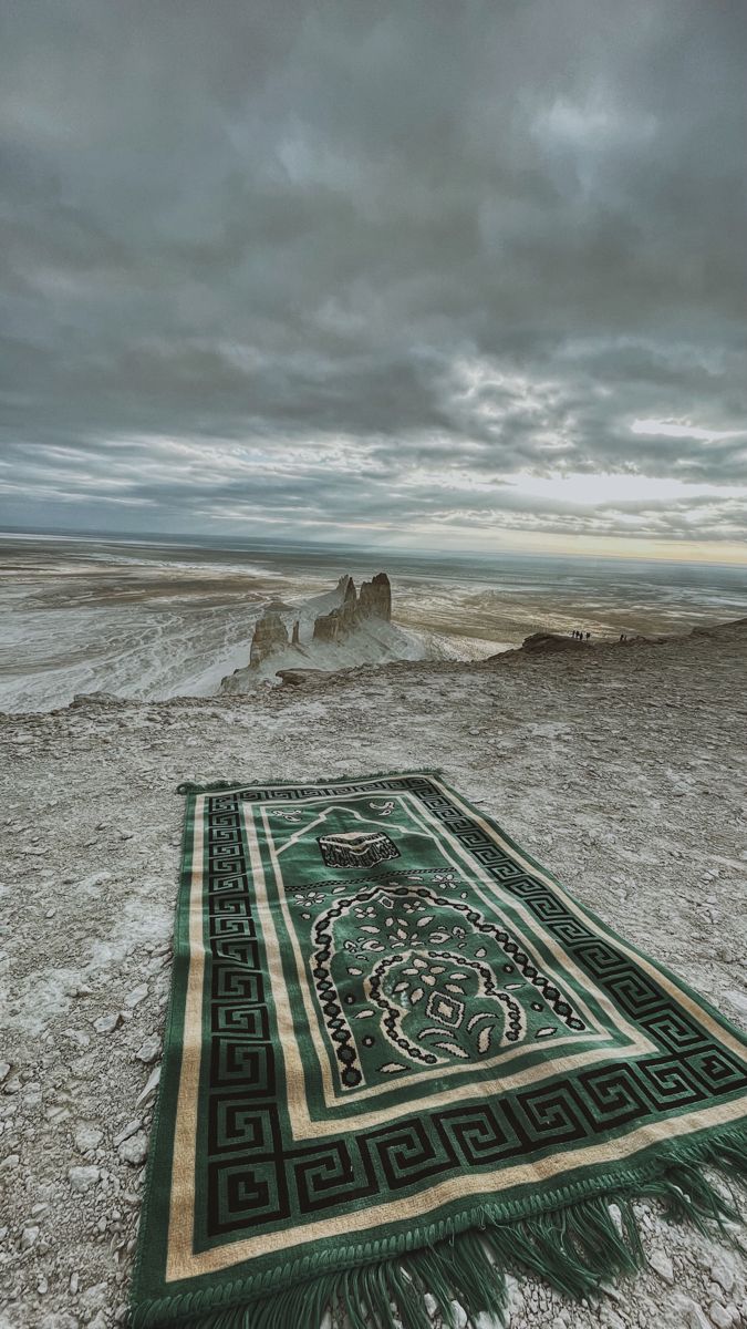 a green and white rug sitting on top of a sandy beach under a cloudy sky