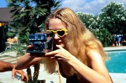 a woman holding up a camera to take a picture with her heart - shaped sunglasses