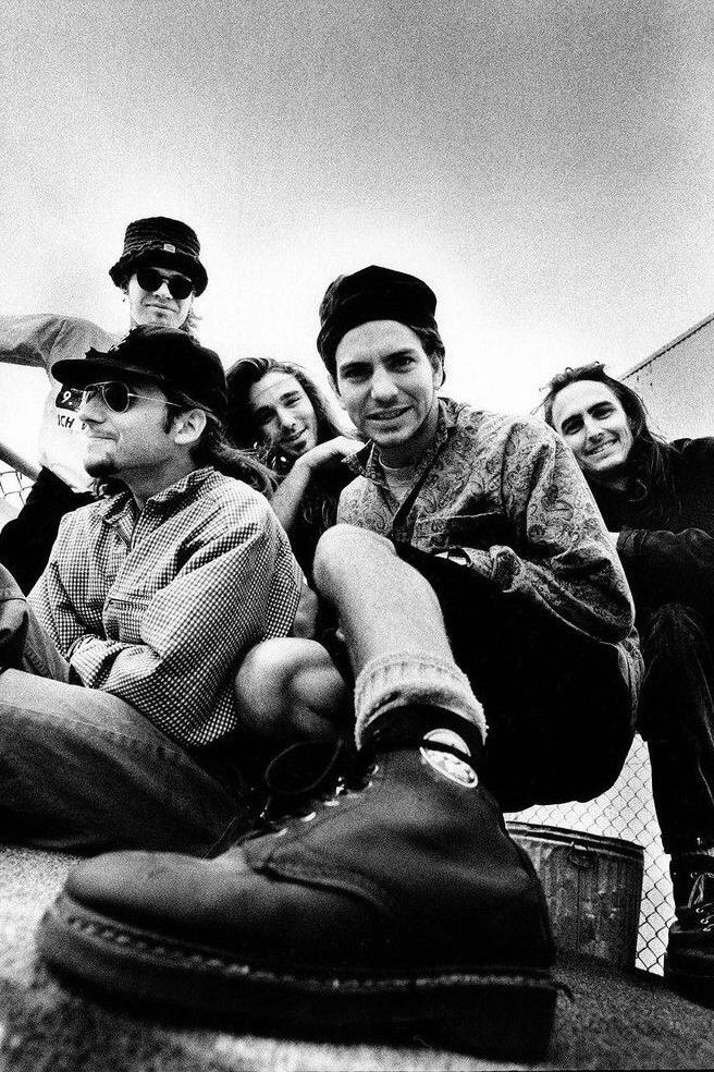 black and white photograph of people sitting on the ground with one person wearing glasses, smiling at the camera