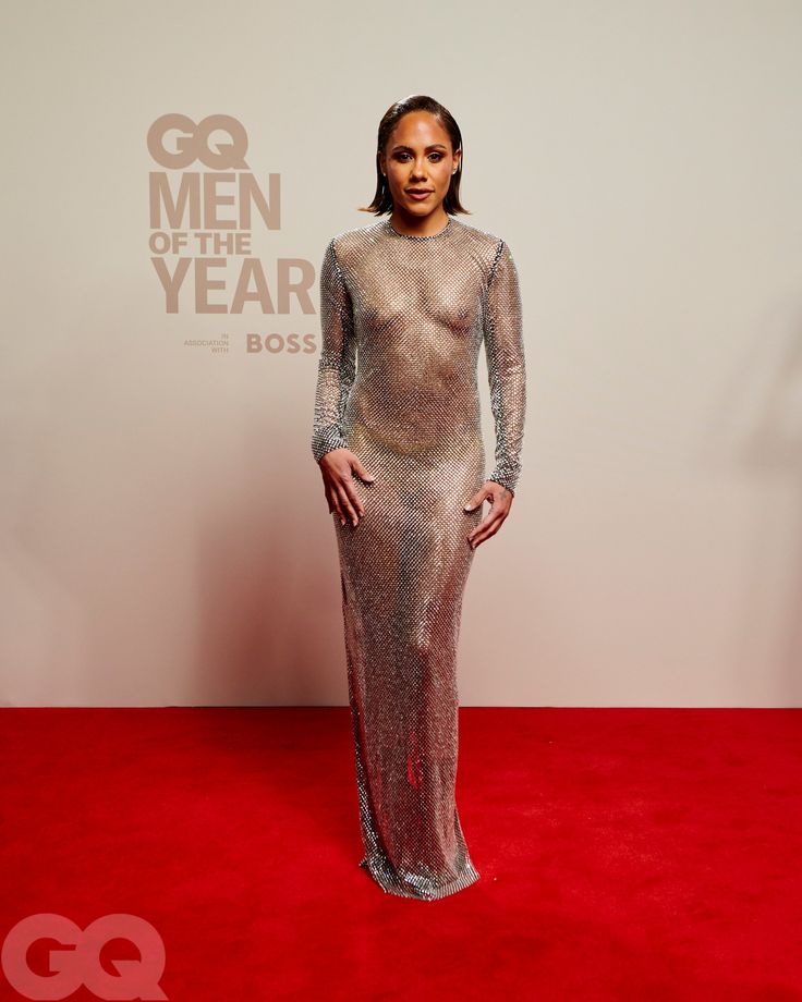 a woman standing on top of a red carpet wearing a silver dress with sheer sleeves